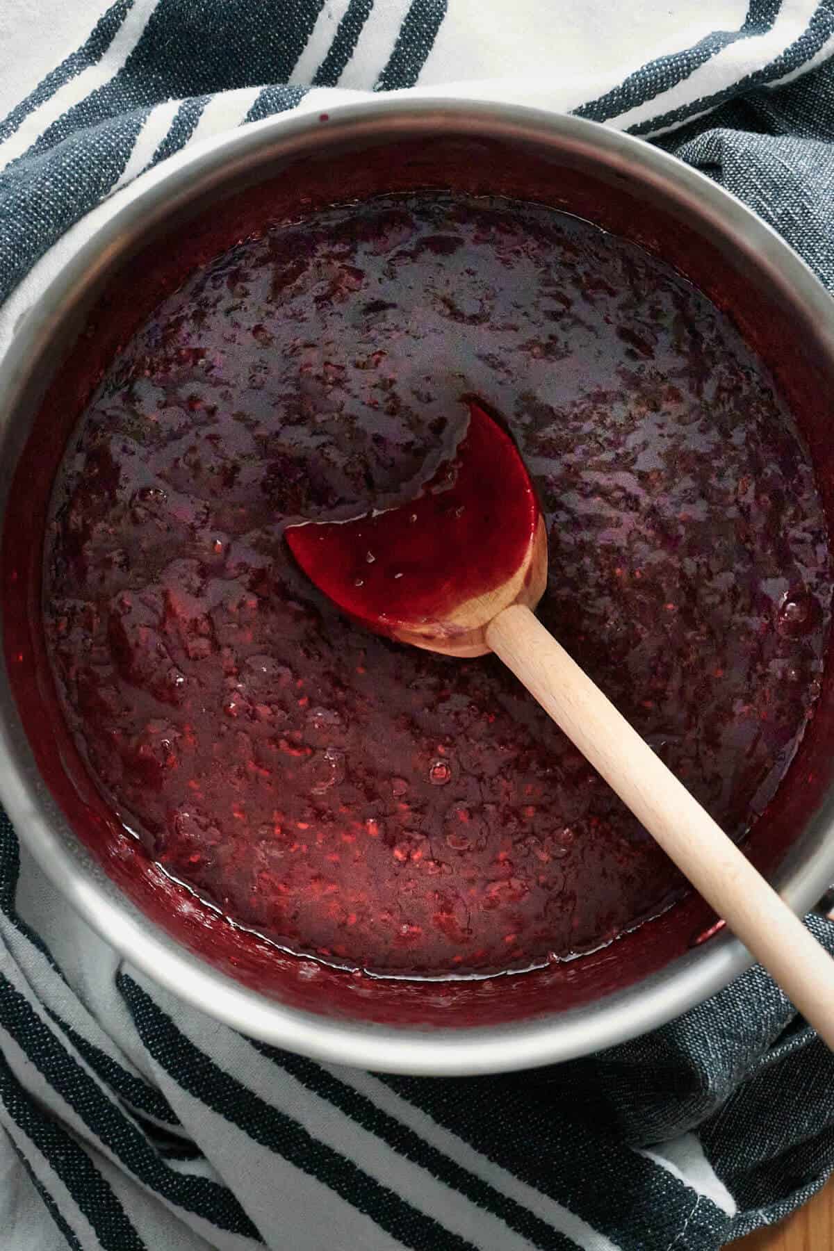 overhead shot of berry sauce in sauce pan with wooden spoon