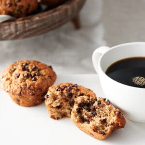 close up of oatmeal chocolate chip muffin split in half with mug of coffee