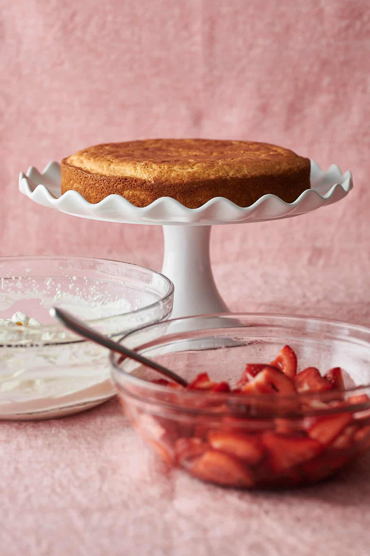 gluten-free shortcake on pedestal cake plate with bowl of whipped cream and bowl of strawberries