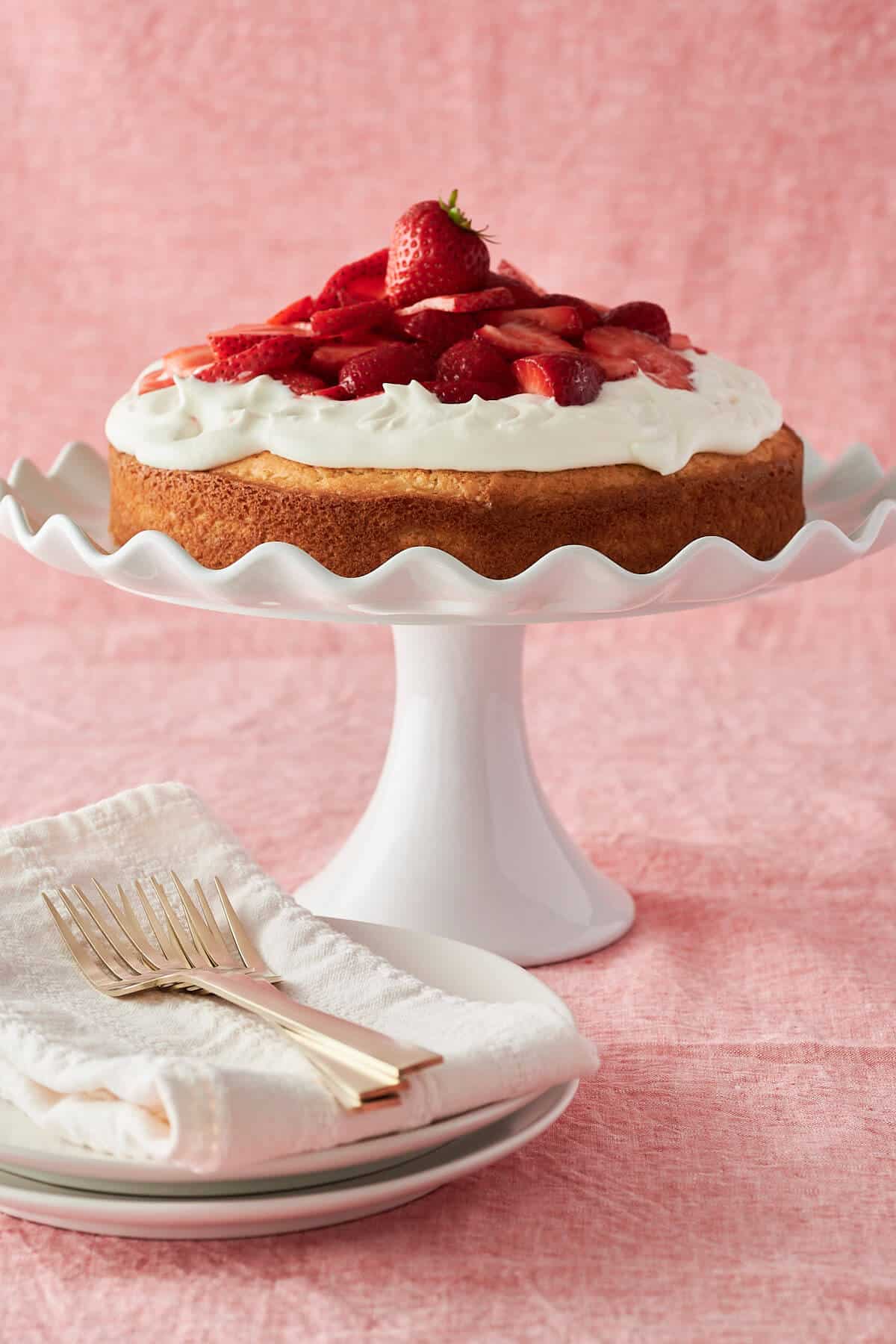 gluten-free shortcake topped with whipped cream and strawberries on pedestal cake plate